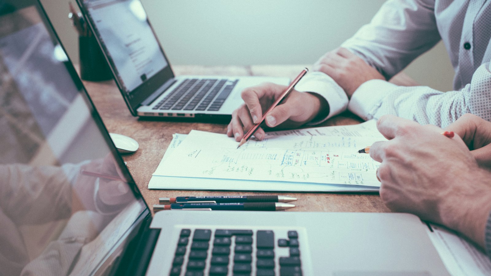 Notizen mit Bleistift neben aufgeklappten Laptops