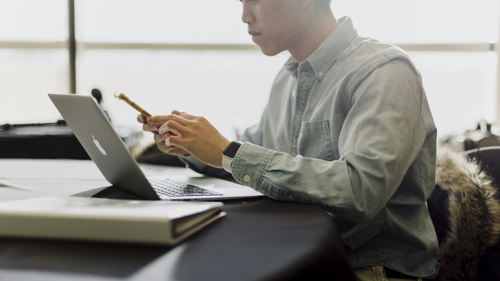 Ein Mitarbeiter mit Smartphone vor seinem Laptop